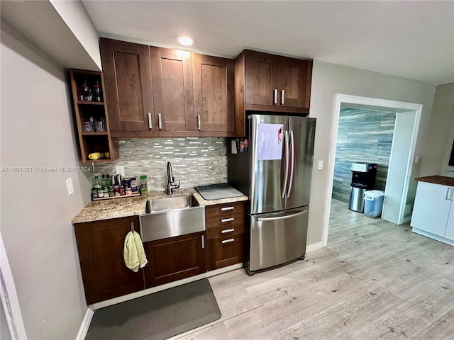 kitchen with light hardwood / wood-style floors, sink, light stone countertops, stainless steel fridge, and decorative backsplash