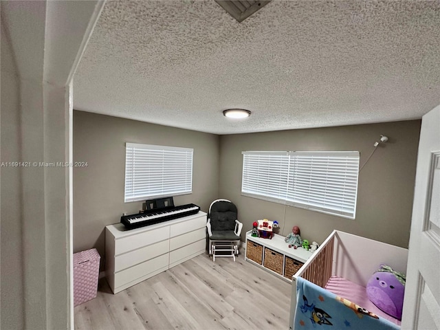 bedroom with a crib, light wood-type flooring, and a textured ceiling