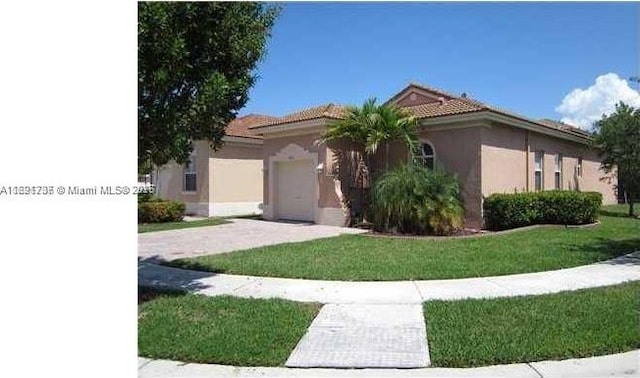 view of front facade featuring a tile roof, stucco siding, a front yard, a garage, and driveway