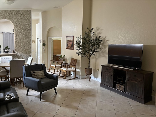 living area featuring baseboards, visible vents, arched walkways, a towering ceiling, and light tile patterned flooring