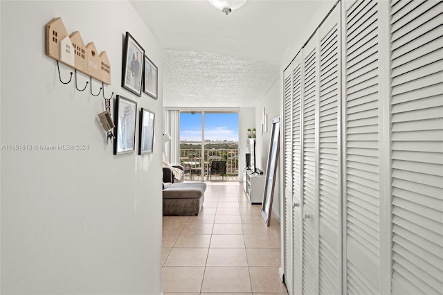 hallway featuring a textured ceiling, light tile patterned flooring, and a wall of windows