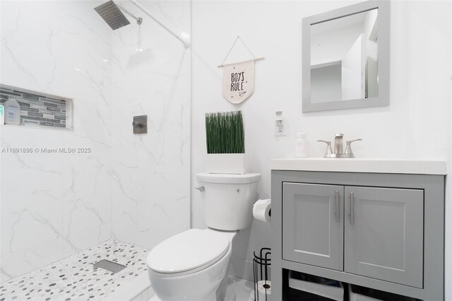 bathroom with a tile shower, vanity, and toilet