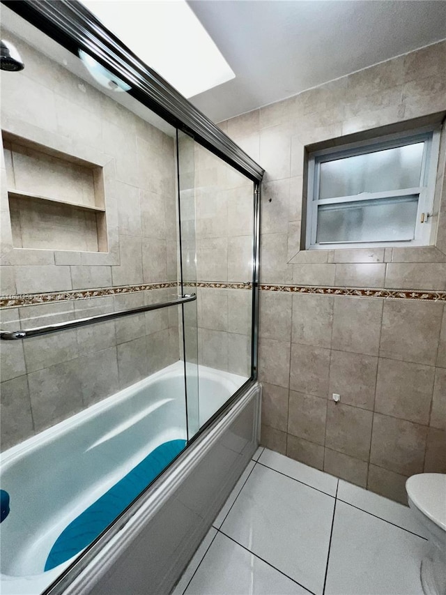 bathroom featuring tile patterned floors, toilet, bath / shower combo with glass door, and tile walls