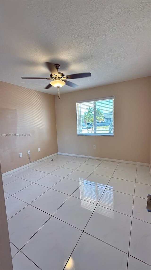 tiled empty room with ceiling fan and a textured ceiling