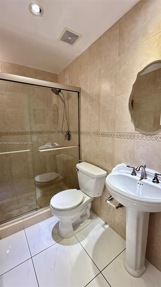 bathroom with an enclosed shower, sink, tile walls, tile patterned flooring, and toilet