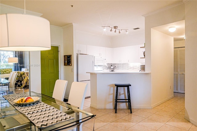 kitchen with kitchen peninsula, white appliances, crown molding, light tile patterned floors, and white cabinets