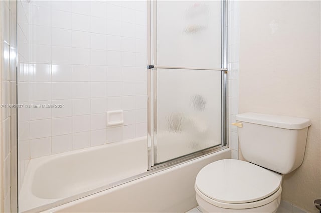 bathroom with toilet and bath / shower combo with glass door