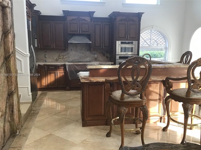 kitchen featuring a kitchen breakfast bar, double oven, extractor fan, decorative backsplash, and light tile patterned floors