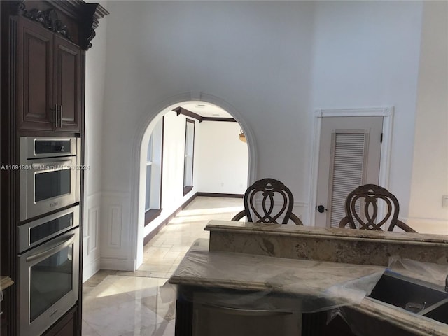 kitchen featuring dark brown cabinets, light stone countertops, and double oven