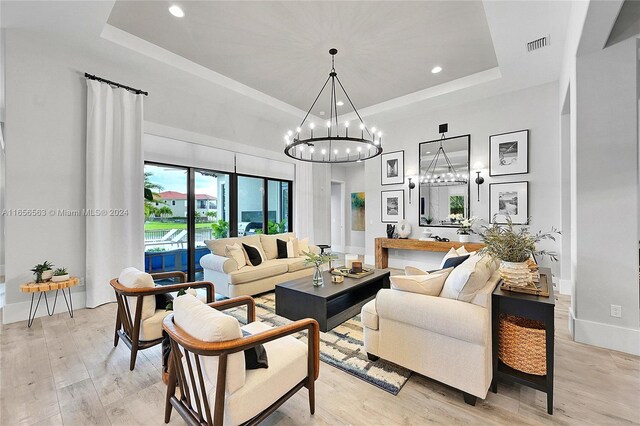 living room featuring an inviting chandelier, light hardwood / wood-style floors, and a raised ceiling