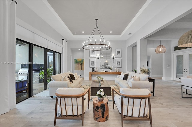 living room with light wood-type flooring, a tray ceiling, french doors, and a notable chandelier