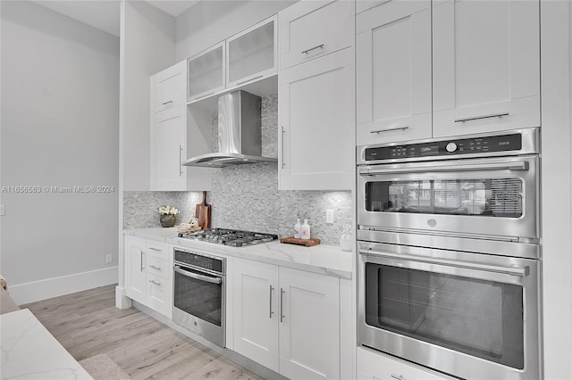 kitchen with white cabinets, stainless steel appliances, light stone counters, and wall chimney range hood