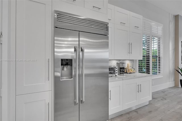 kitchen featuring white cabinetry, decorative backsplash, stainless steel built in fridge, and light hardwood / wood-style flooring