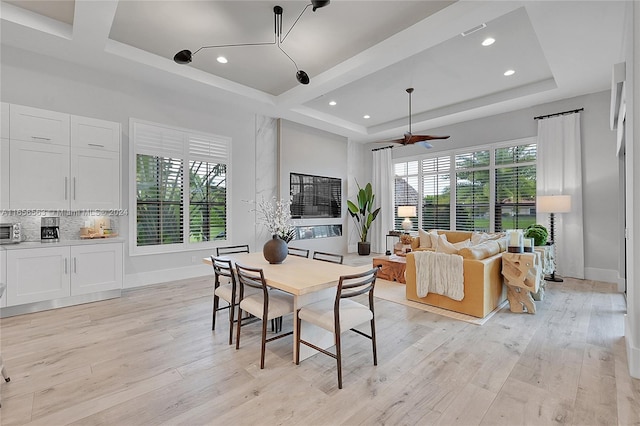 dining area with light wood-type flooring, a wealth of natural light, ceiling fan, and a raised ceiling