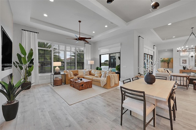 living room featuring light hardwood / wood-style floors, ceiling fan with notable chandelier, and a raised ceiling