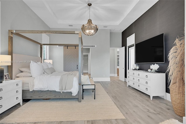 bedroom featuring a tray ceiling, a barn door, a notable chandelier, and light hardwood / wood-style floors