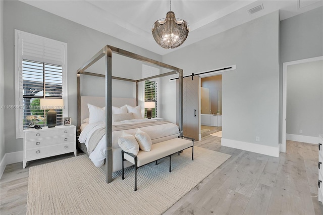 bedroom featuring a barn door, an inviting chandelier, light hardwood / wood-style flooring, and ensuite bathroom