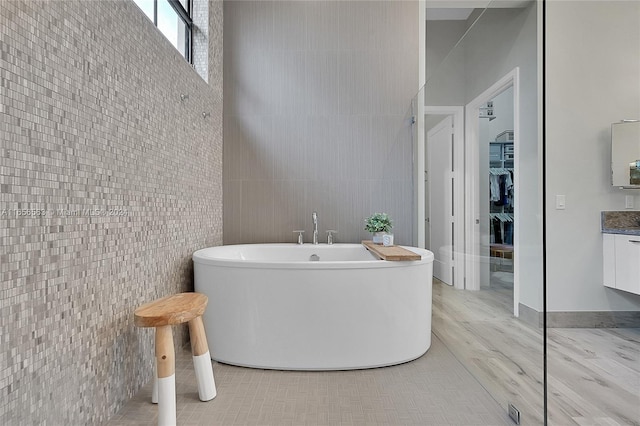 bathroom with hardwood / wood-style flooring, vanity, tile walls, and a tub