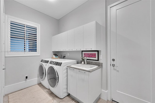 clothes washing area featuring cabinets, sink, light wood-type flooring, and washing machine and clothes dryer