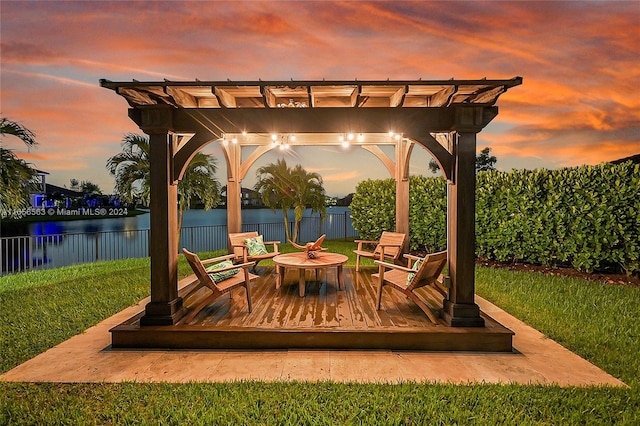 patio terrace at dusk with a deck with water view, a lawn, and a pergola