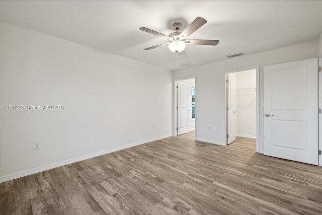 unfurnished bedroom featuring ceiling fan, a closet, a walk in closet, and light hardwood / wood-style flooring