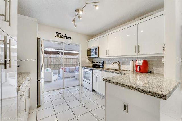 kitchen featuring kitchen peninsula, appliances with stainless steel finishes, light stone countertops, sink, and white cabinetry