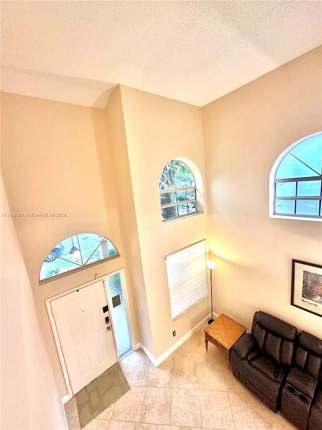 foyer entrance with light tile patterned floors, a towering ceiling, and a textured ceiling