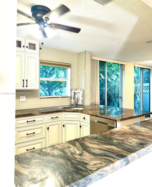 kitchen featuring dishwasher, backsplash, sink, dark stone countertops, and a textured ceiling