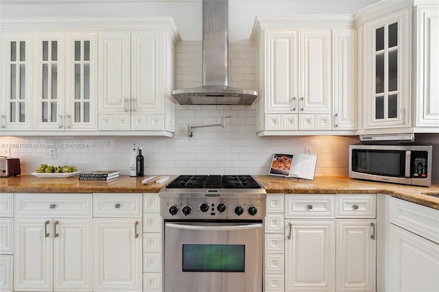 kitchen with backsplash, white cabinets, wall chimney exhaust hood, light stone countertops, and appliances with stainless steel finishes