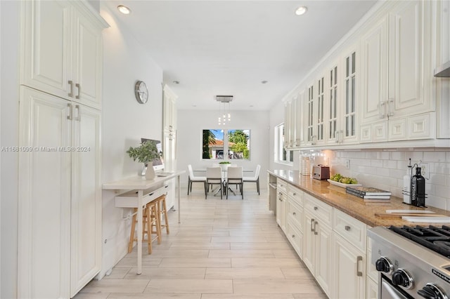 kitchen featuring light stone countertops, hanging light fixtures, stainless steel range with gas cooktop, backsplash, and white cabinets