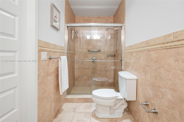 bathroom featuring tile patterned floors, toilet, a shower with shower door, and tile walls