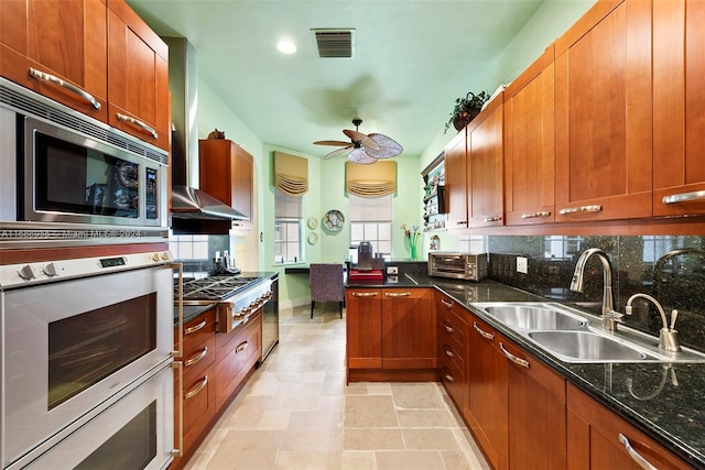 kitchen with sink, appliances with stainless steel finishes, dark stone counters, wall chimney exhaust hood, and decorative backsplash