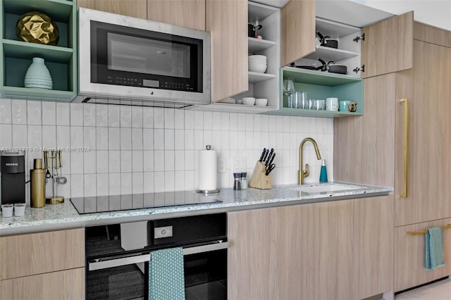 kitchen featuring stainless steel appliances, sink, light stone counters, light brown cabinets, and decorative backsplash