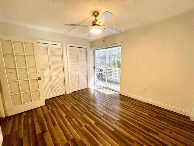 unfurnished bedroom with access to outside, a textured ceiling, dark hardwood / wood-style flooring, multiple closets, and ceiling fan