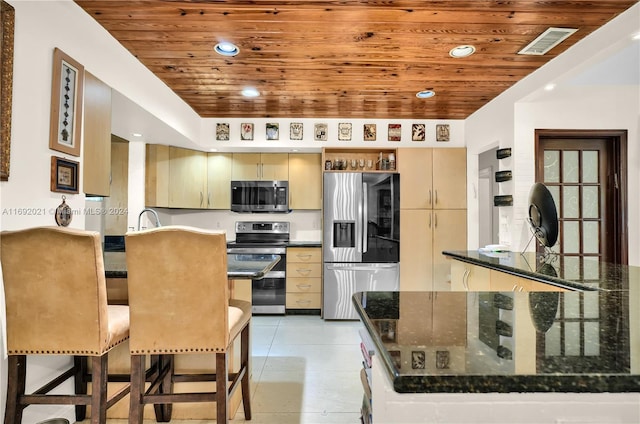 kitchen with stainless steel appliances, wooden ceiling, a kitchen bar, and dark stone counters