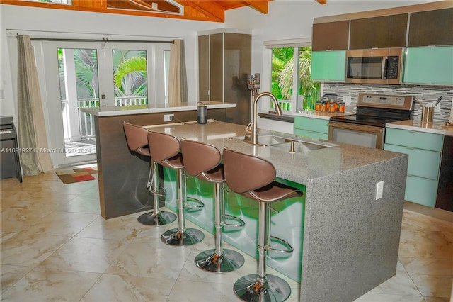 kitchen with beam ceiling, a wealth of natural light, a center island with sink, and electric range