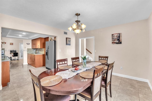 dining room with ornamental molding, a textured ceiling, a raised ceiling, an inviting chandelier, and sink