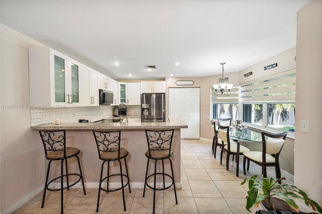 kitchen featuring a chandelier, stainless steel appliances, light stone countertops, white cabinets, and kitchen peninsula