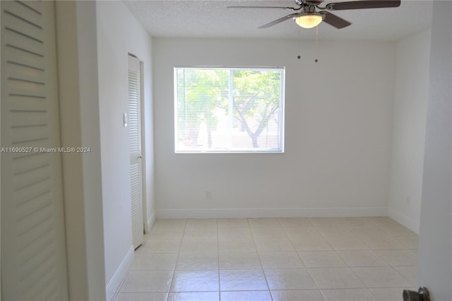 empty room with a textured ceiling, light tile patterned floors, and ceiling fan