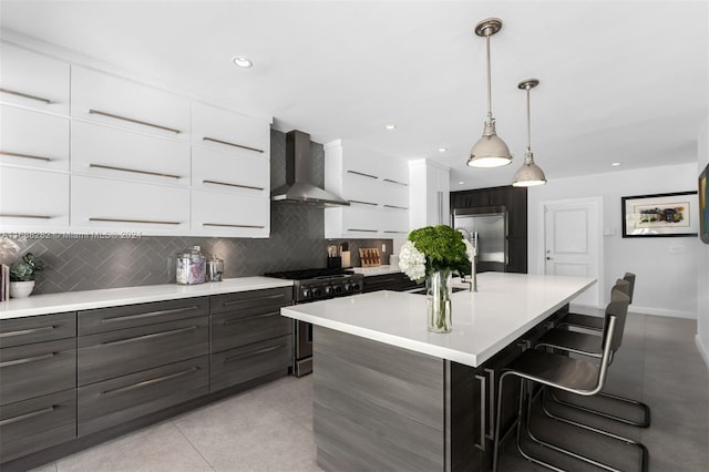 kitchen featuring a center island with sink, white cabinetry, wall chimney range hood, and high quality appliances