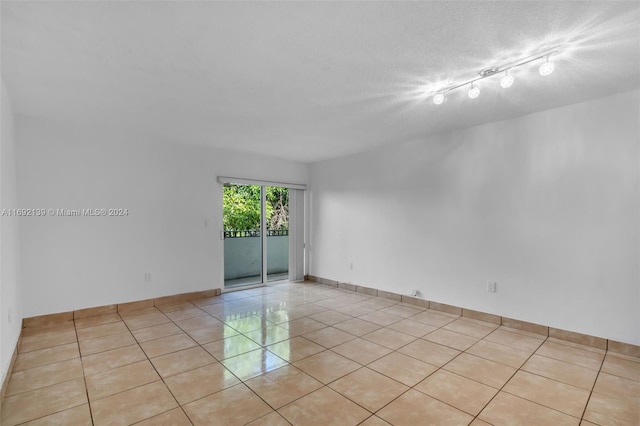 empty room featuring light tile patterned flooring, rail lighting, and a textured ceiling