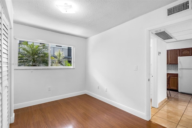 spare room featuring a textured ceiling and light hardwood / wood-style floors