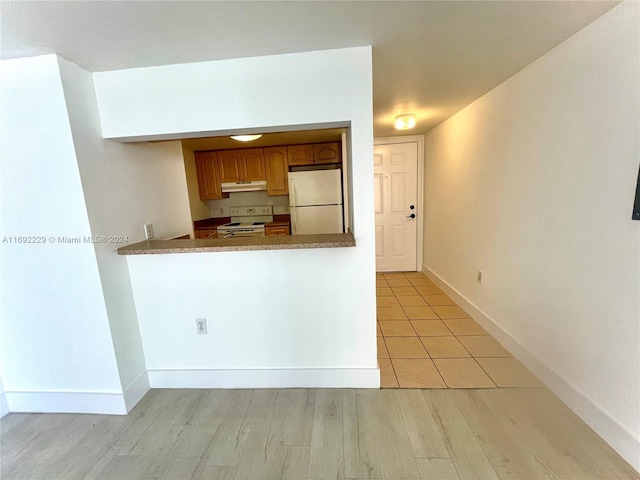 kitchen with kitchen peninsula, white appliances, and light wood-type flooring