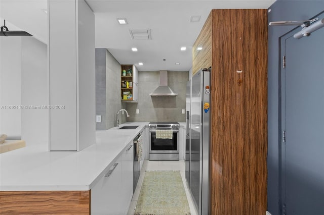 kitchen featuring stainless steel appliances, white cabinetry, wall chimney range hood, light tile patterned floors, and sink