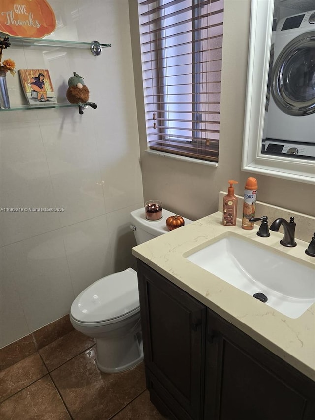 bathroom featuring vanity, stacked washing maching and dryer, tile patterned floors, and toilet