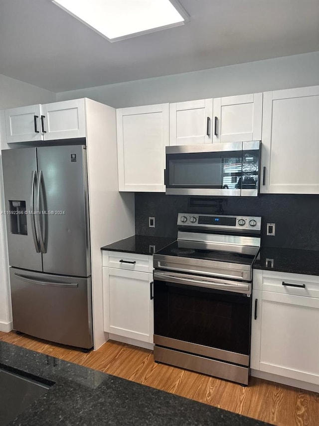 kitchen featuring backsplash, appliances with stainless steel finishes, dark stone counters, white cabinets, and light wood-type flooring