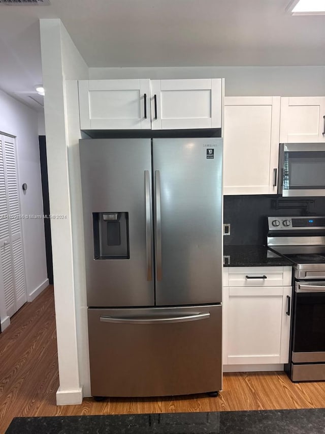 kitchen with white cabinets, appliances with stainless steel finishes, backsplash, and light hardwood / wood-style floors