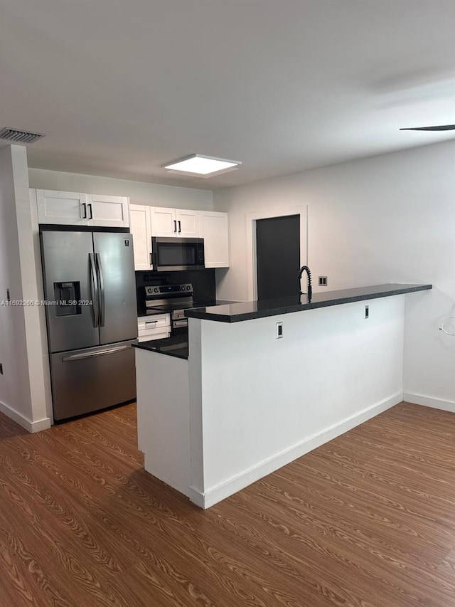 kitchen with kitchen peninsula, appliances with stainless steel finishes, dark wood-type flooring, sink, and white cabinetry