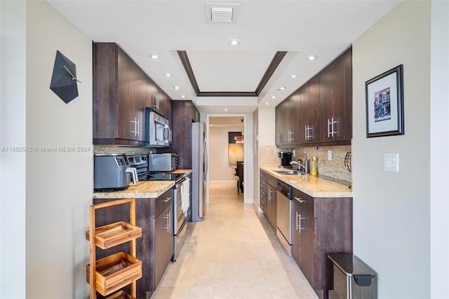 kitchen with stainless steel appliances, sink, dark brown cabinets, a raised ceiling, and decorative backsplash