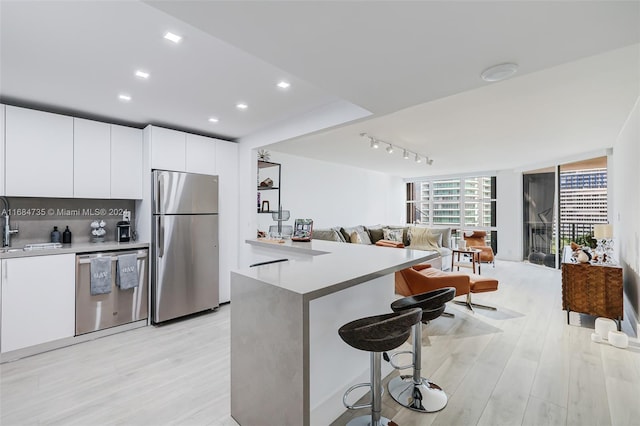 kitchen featuring stainless steel appliances, a kitchen bar, white cabinetry, and light wood-type flooring